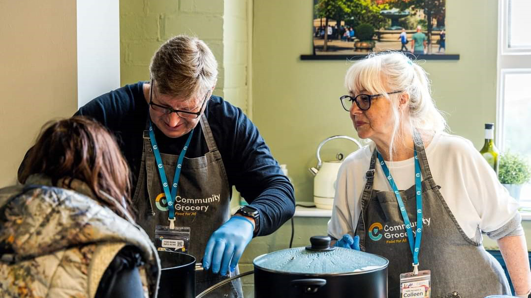 two people serving soup to a member of the community