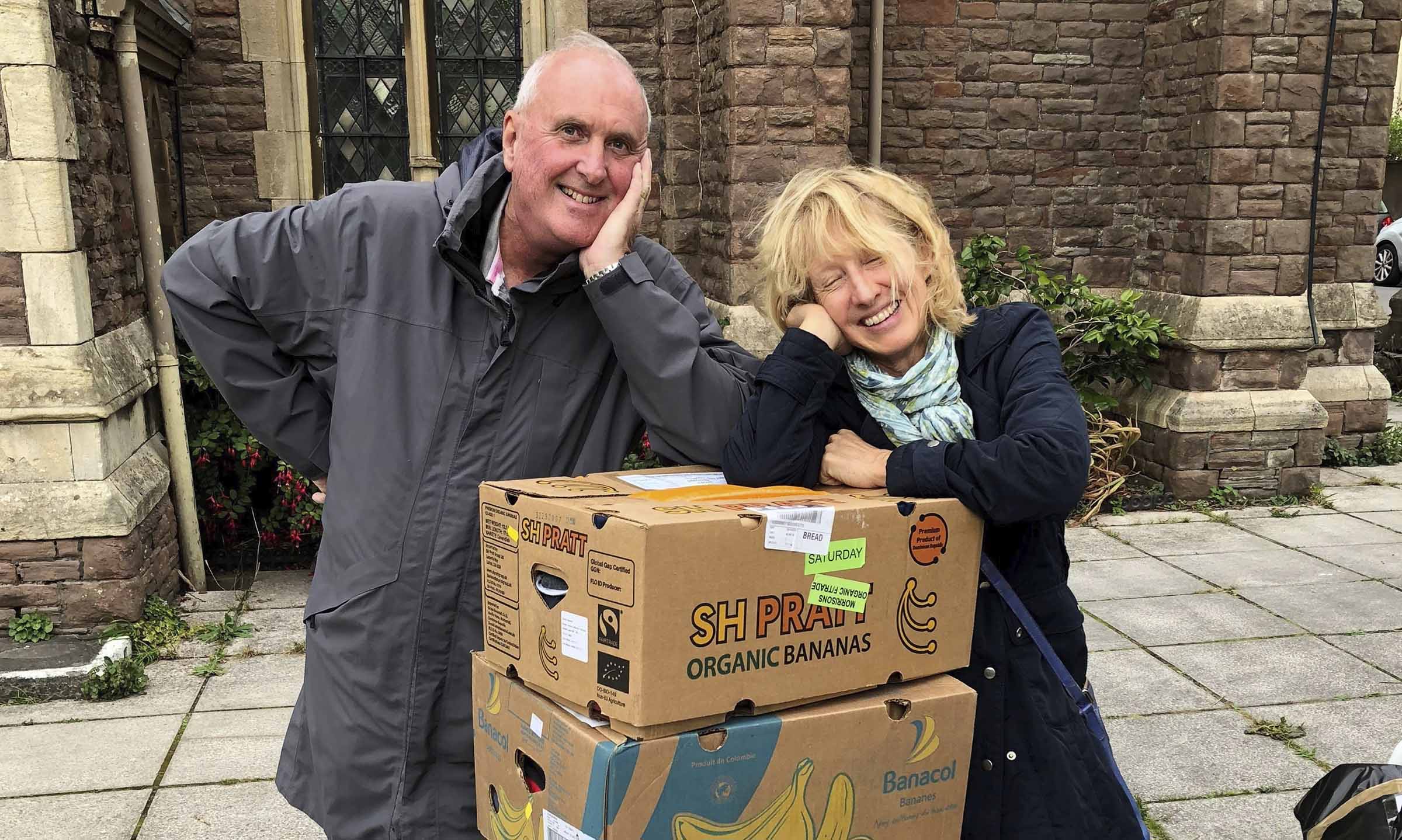 Man and woman outside church with boxes of bananas