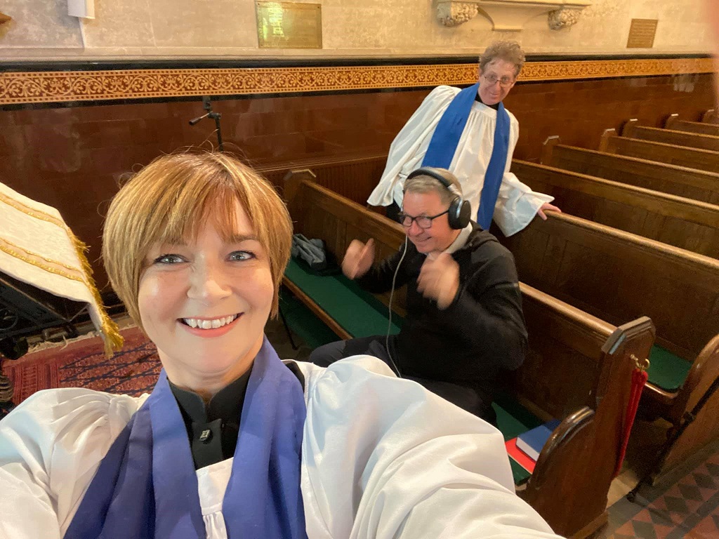 Female vicar taking selfie with two others in church pews
